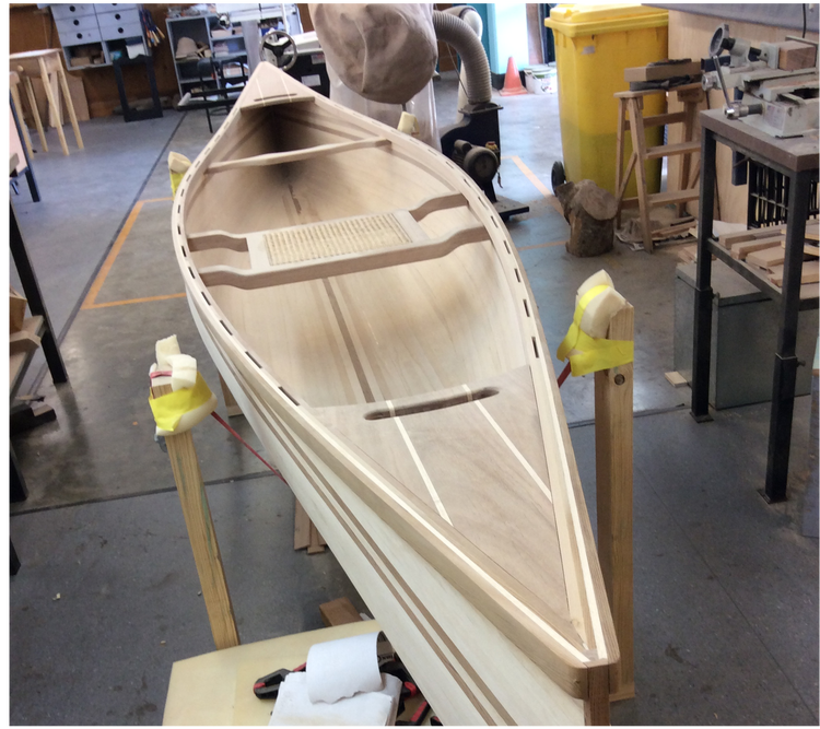 An intricate handcrafted wooden canoe supported on wooden stands in a workshop environment.